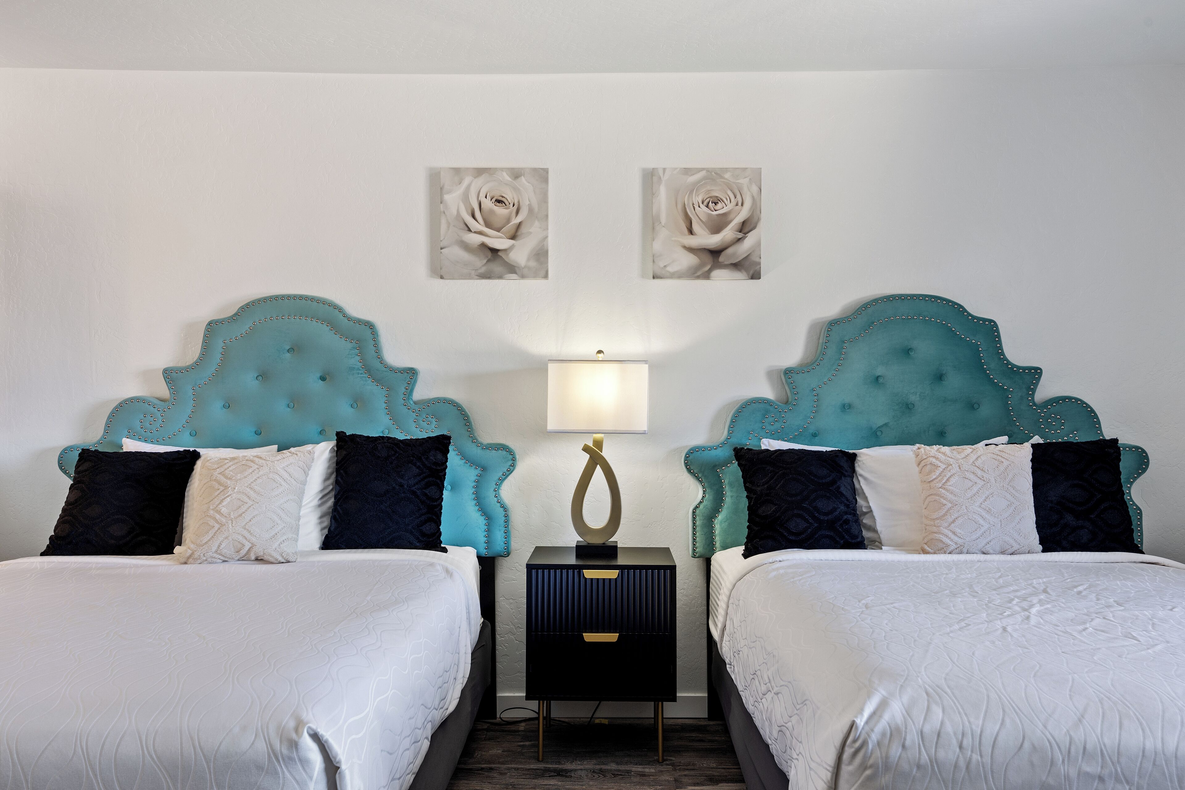 A double room with two beds, each with a teal headboard, white bedding, and a small bedside table with a lamp.