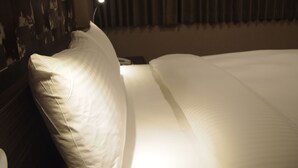 A neatly made bed with white linens and a single pillow, a bedside lamp, and a dark curtain in the background. - Fairytale YiSu Hot Spring Hotel (Jiaoxi)