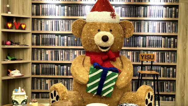 A library with a large teddy bear wearing a Santa hat, surrounded by various animal-shaped cushions on a colorful checkered floor. - Fairytale YiSu Hot Spring Hotel (Jiaoxi)