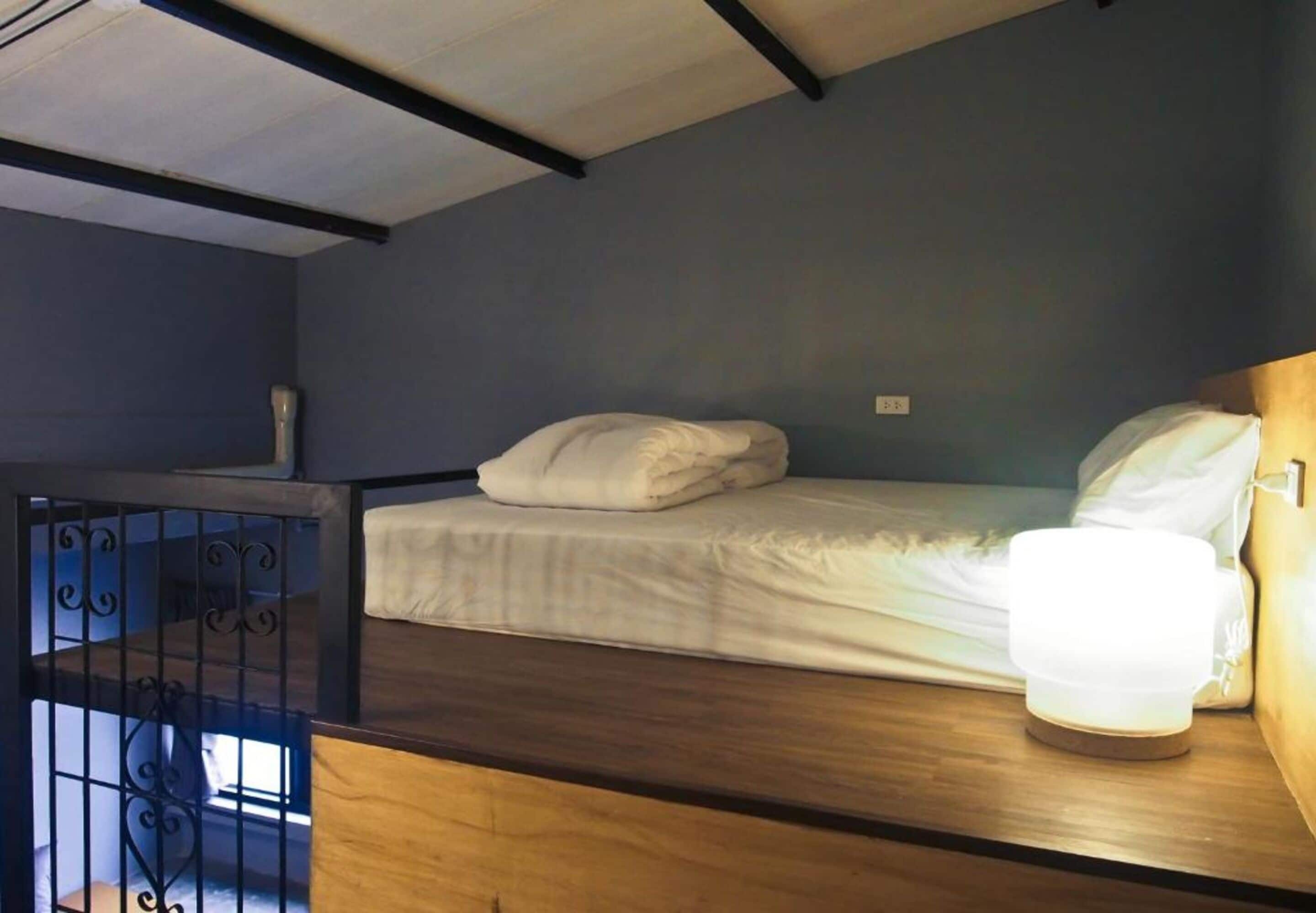 A single bed with white bedding in a room with a dark blue wall and a wooden headboard.