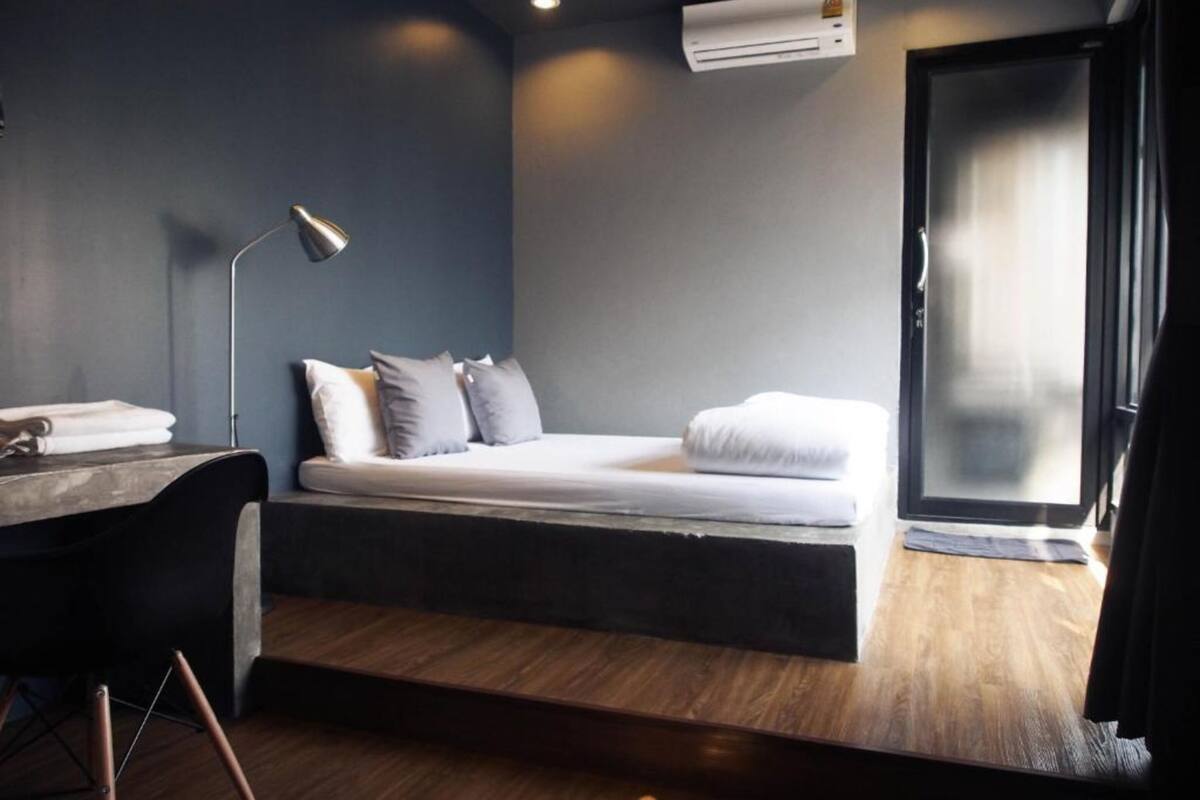 A modern bedroom with a bed, bedside table, lamp, and an air conditioning unit.