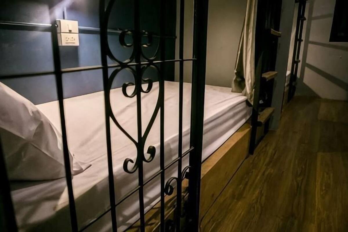 A single bed with a metal frame, a wooden floor, and a wall-mounted electrical outlet.
