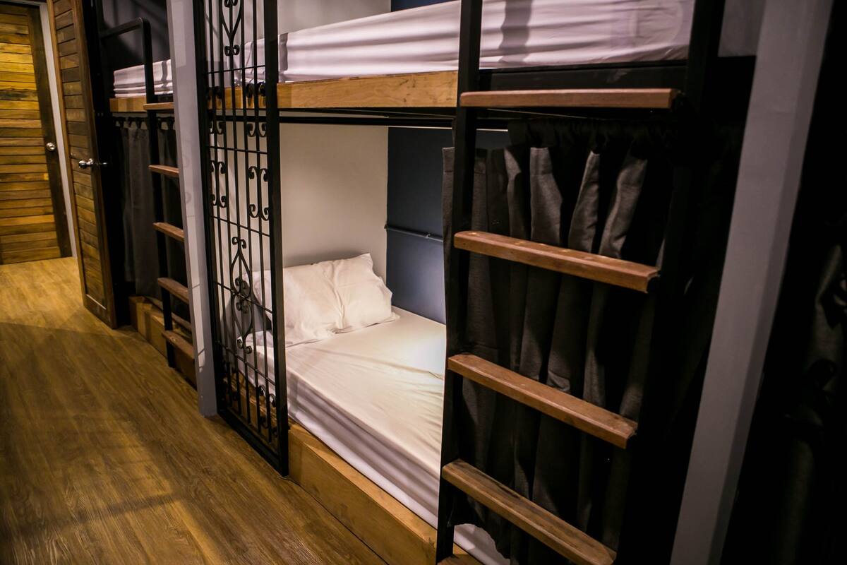 A bunk bed room with a wooden floor, a metal gate, and a shelf with clothes.