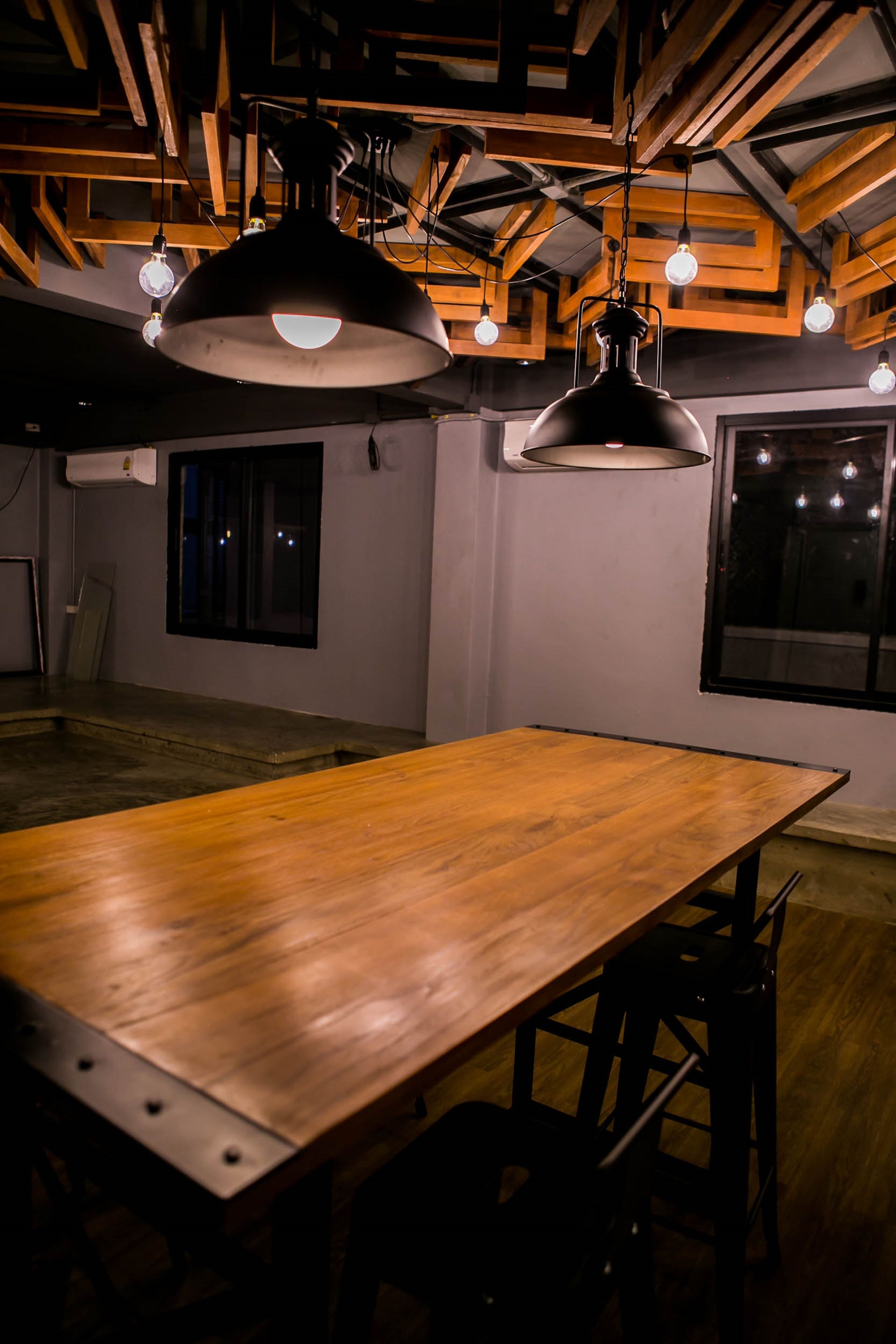 A spacious room with a long wooden table and hanging pendant lights.