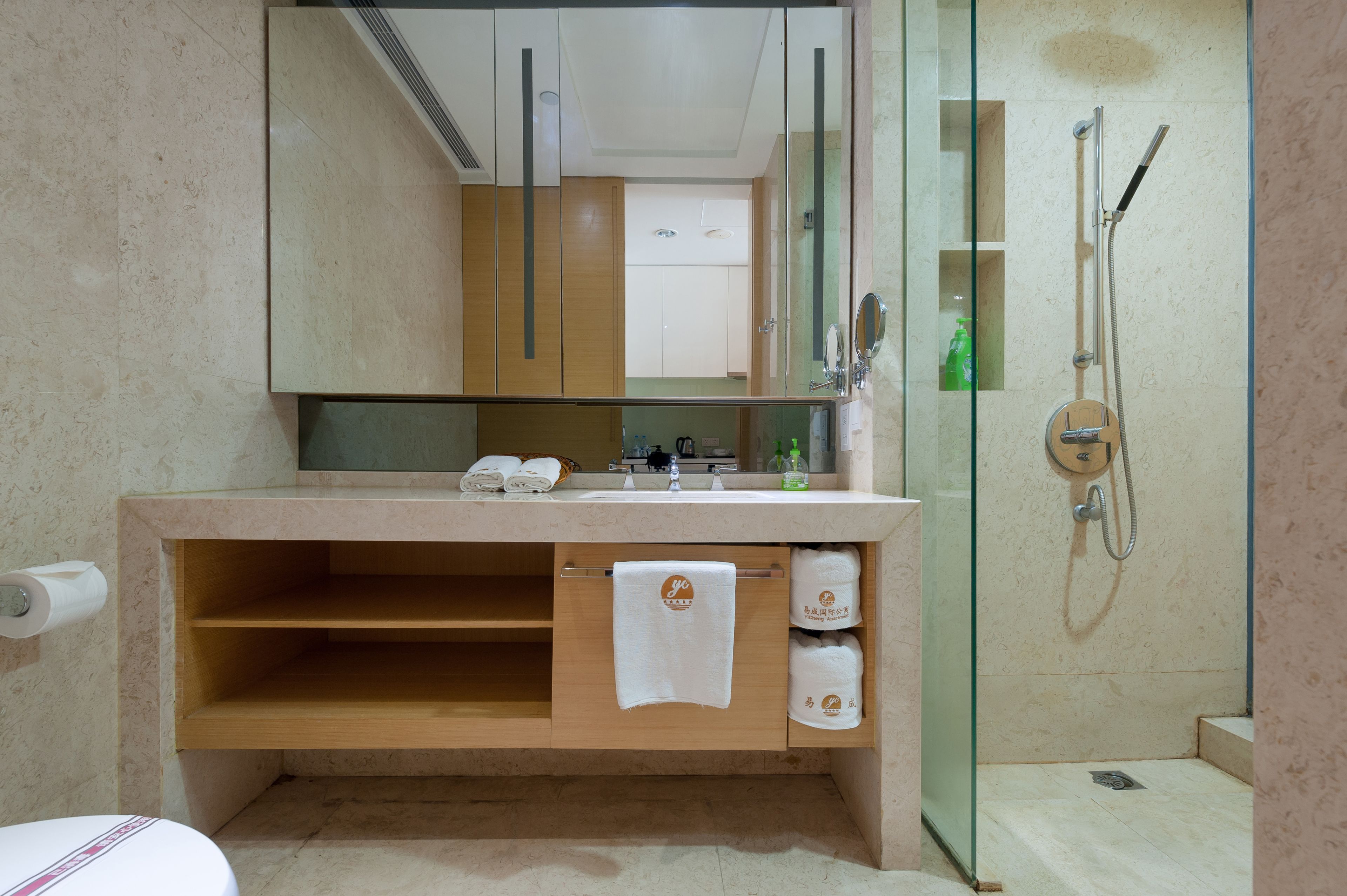 Une salle de bain dotée d’une douche à parois de verre, d’un meuble-lavabo en bois avec un porte-serviettes et d’un miroir au-dessus du lavabo.