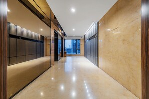 A modern, well-lit hallway with a polished floor, large windows, and a view of the cityscape.