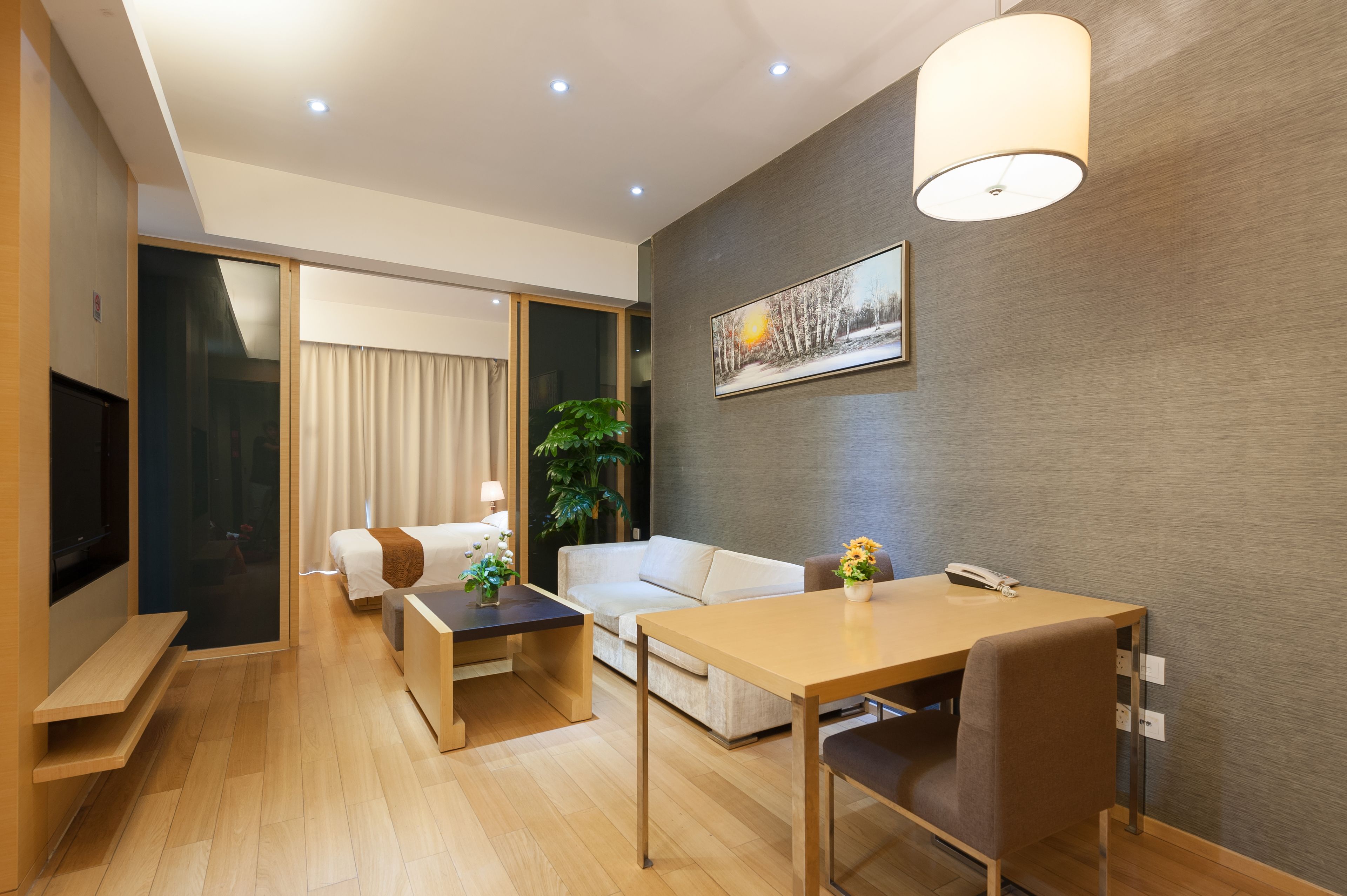 A modern hotel room with a bed, a sofa, a dining table, and a TV.