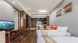 Moderni hotellihuone, jossa on suuri taulutelevisio, sohva, sänky ja ruokailutila.