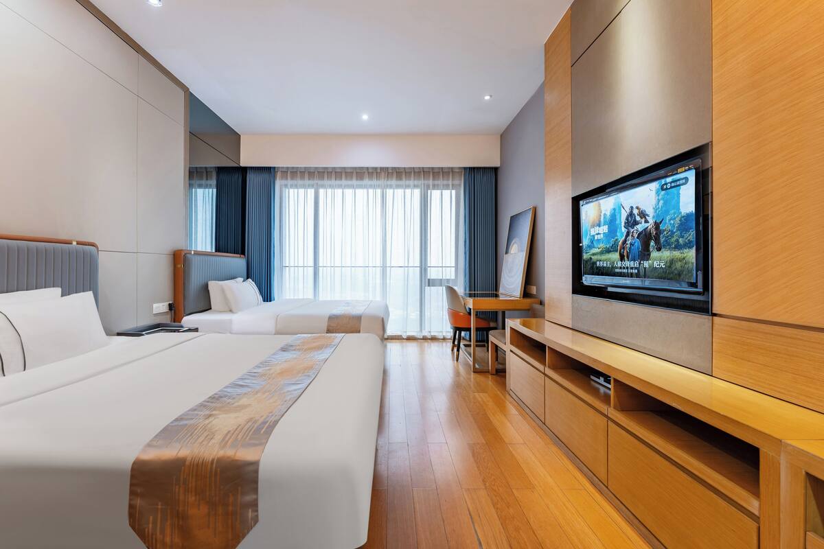 Moderni hotellihuone, jossa on suuri sänky, työpöytä ja seinälle asennettu televisio.