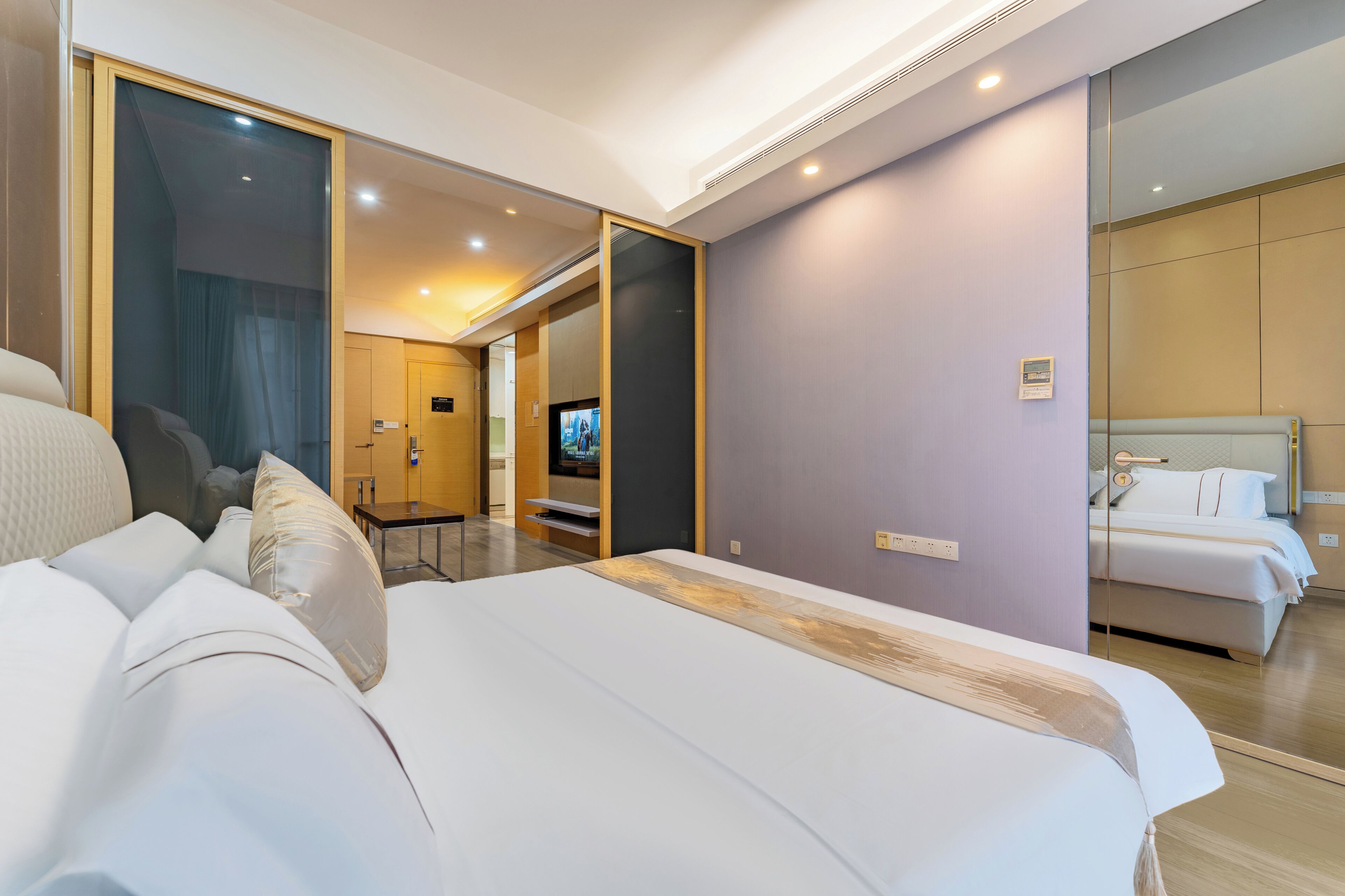 A modern hotel room with a large bed, a TV, and a separate sleeping area.