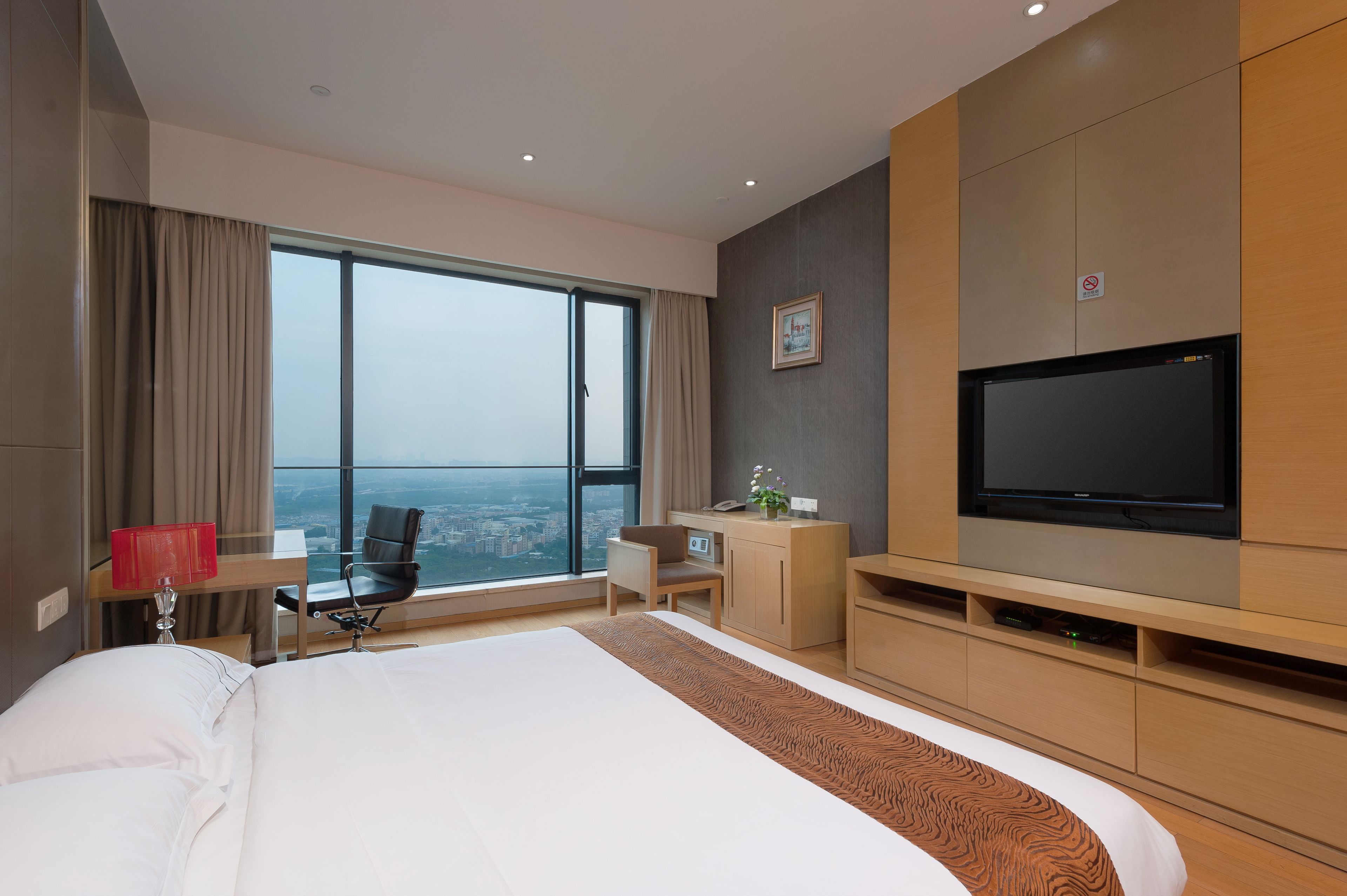 Una moderna camera d'hotel con un letto grande, una scrivania con una sedia, una televisione e vista sulla città da una grande finestra.