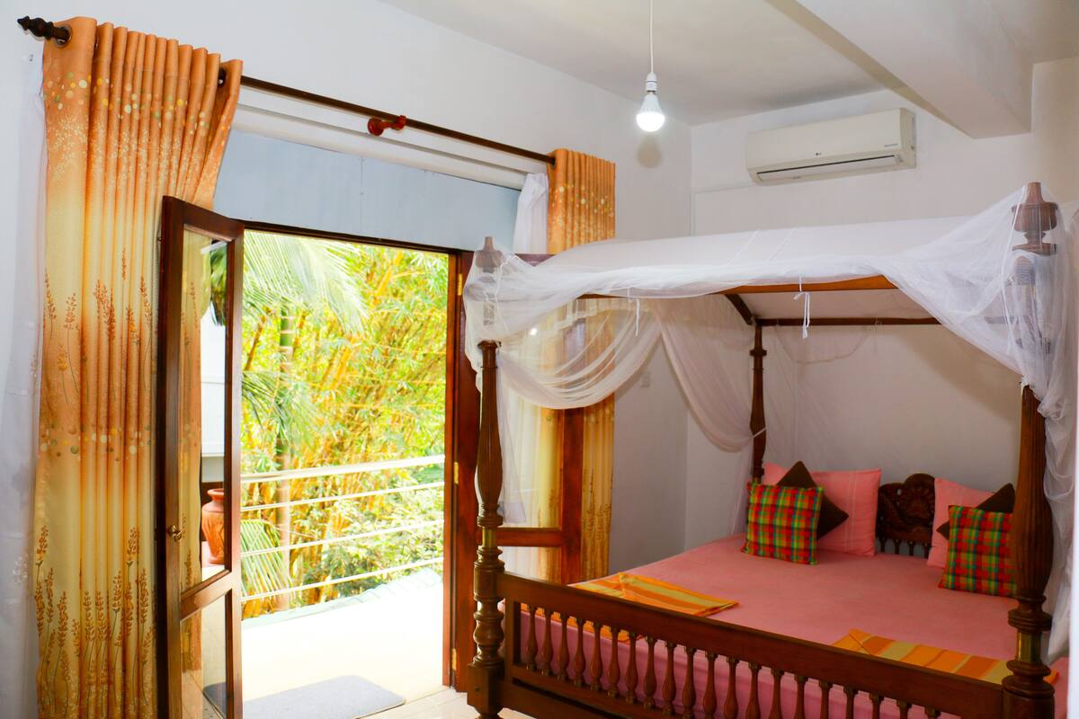A bedroom with a four-poster bed, a balcony with curtains, and an air conditioning unit on the wall.
