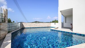 Ein moderner Außenpool mit glasklarer, blauer Wasserfläche, umgeben von einem weißen Gebäude und einer Steinmauer.