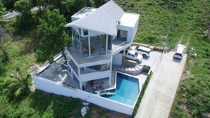 Ein modernes, mehrstöckiges Haus mit Pool, umgeben von viel Grün.