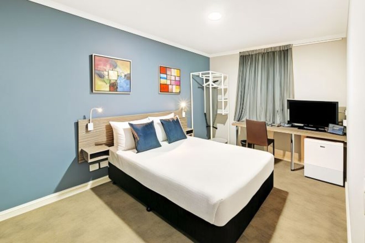 Een hotelkamer met een bed, bureau, televisie en kunst aan de wanden.