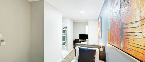 A hotel room with a bed, a desk with a computer, a TV, and a large painting on the wall.