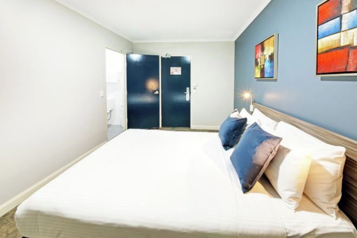 A hotel room with a large bed, two doors, and artwork on the wall.