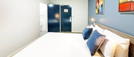 A hotel room with a large bed, two doors, and a wall with a painting.