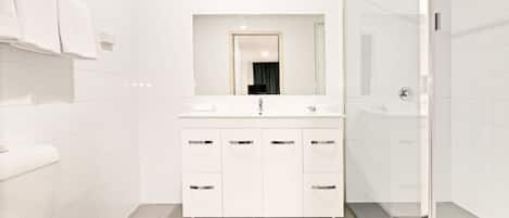 A modern bathroom with a white toilet, a sink with a mirror above it, and a shower area.