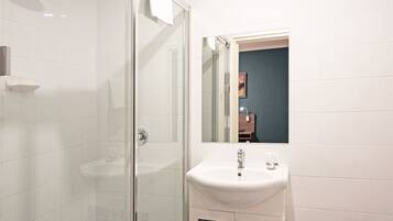 A modern bathroom with a glass shower enclosure, a white sink, and a mirror reflecting a dark wall and a small piece of artwork.