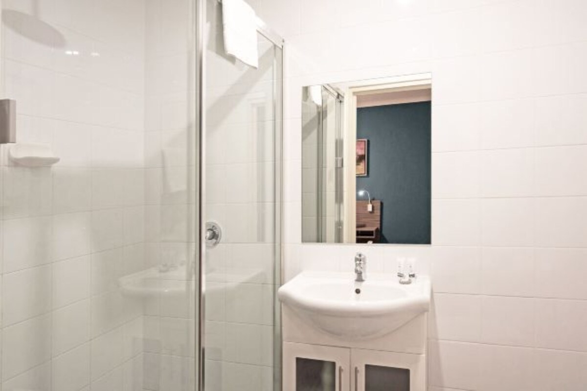 Een badkamer met een douchecabine van glas, een wit wastafeltje en een spiegel erboven.