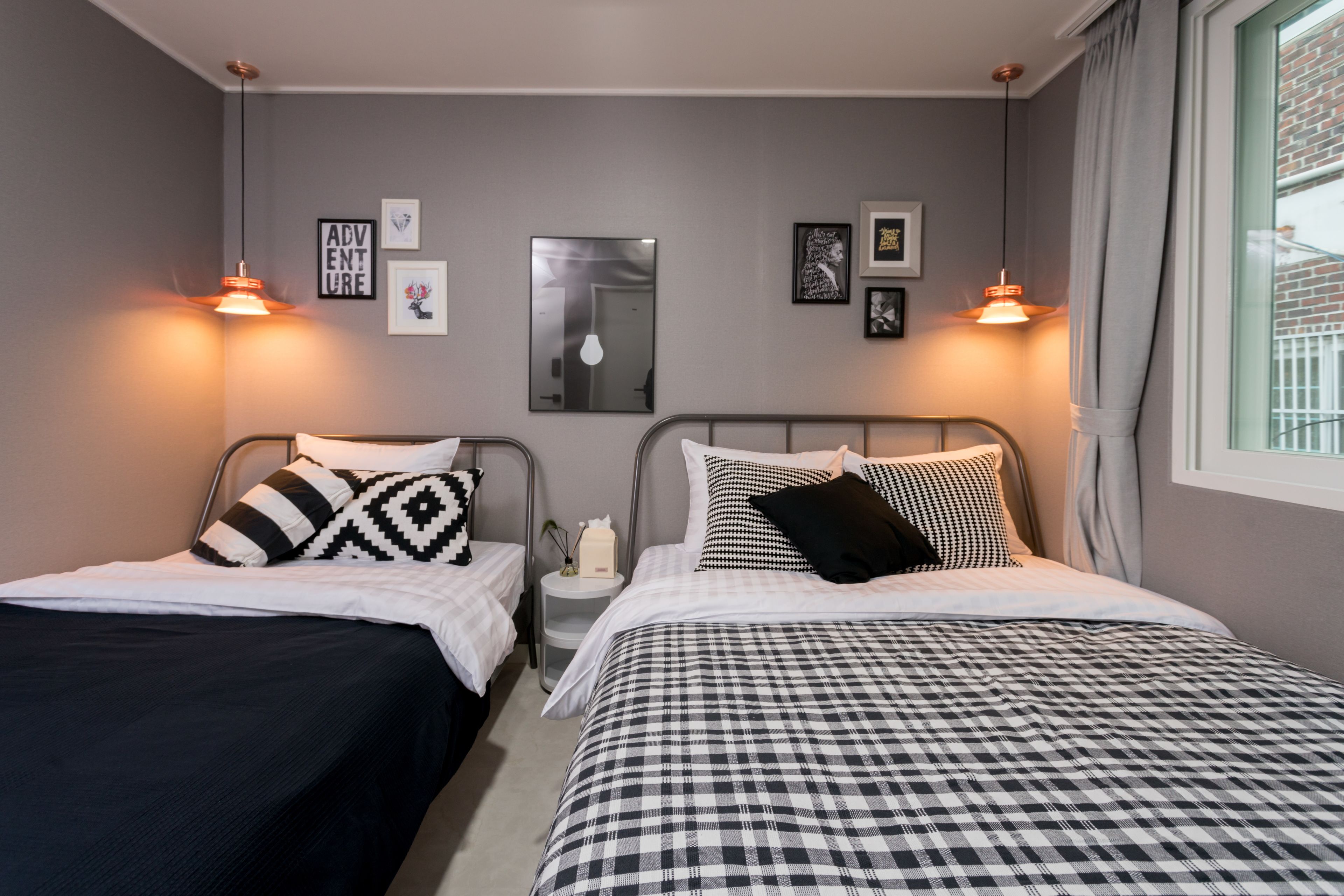 A bedroom with two beds, each with a distinct black and white checkered bedspread. There are wall-mounted lights and framed pictures on the wall.