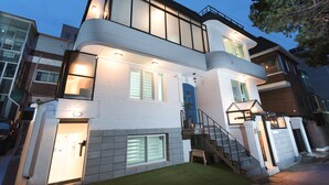 A modern two-story house with a white exterior, a blue door, and a staircase leading to the upper floor. - Neat House (Seoul)