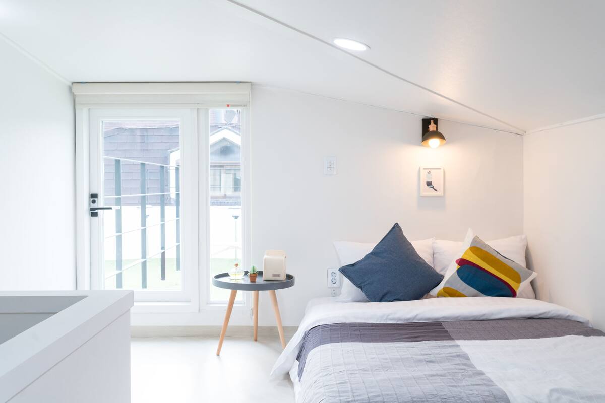 A modern bedroom with a bed, bedside table, and a view through a sliding door to the outside.