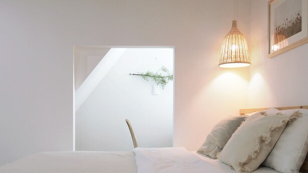 A bedroom with a bed, a chair, a hanging plant, and a wall-mounted light fixture. - Neat House (Seoul)