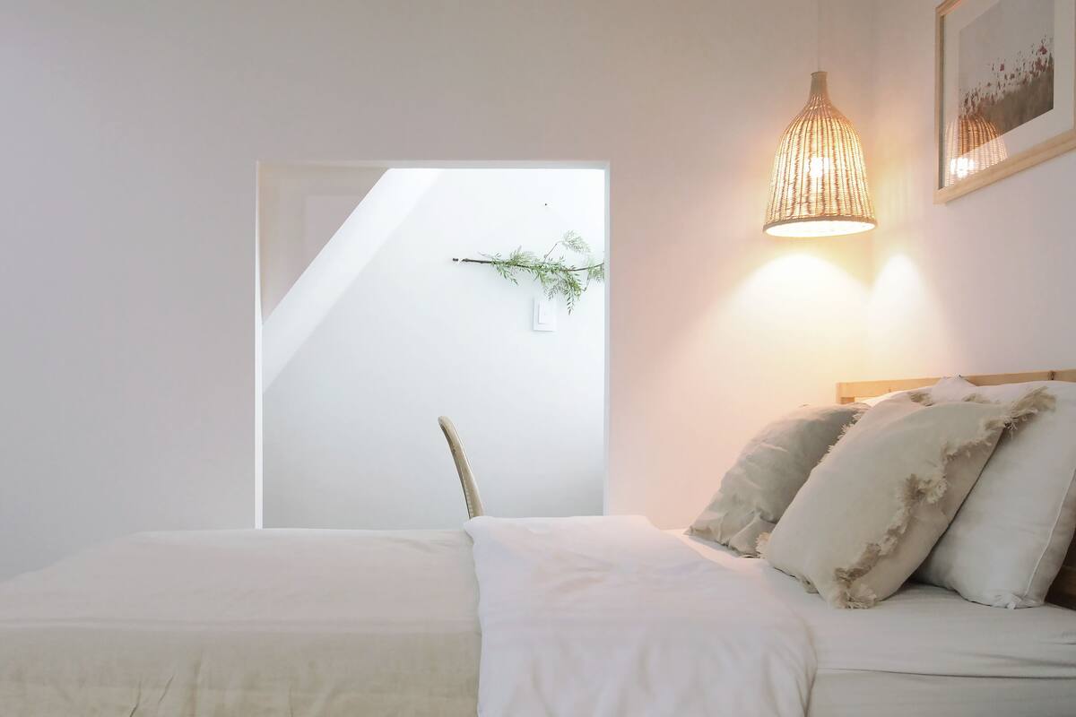 A bedroom with a bed, a chair, a hanging plant, and a wall-mounted light fixture.