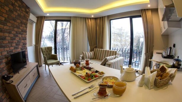 A modern living room with a dining area, a sofa set, a television, and a breakfast spread on the table. - Aldino Residence (Ankara)