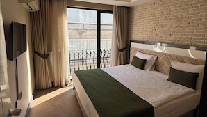 A modern hotel room with a large bed, a TV, a balcony with a view, and a brick wall. - Aldino Residence (Ankara)