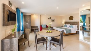 A hotel room with a bed, a dining table with chairs, a TV mounted on the wall, and a small seating area with a bench and a couch. - Sterling Goa Varca (Varca)