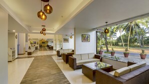 A spacious lobby with a central seating area, a reception desk, and a view of palm trees outside. - Sterling Goa Varca (Varca)
