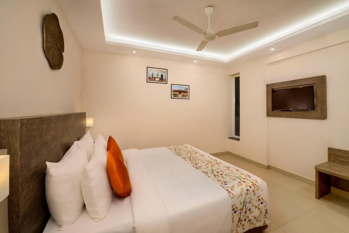 A hotel room with a bed, a ceiling fan, a TV mounted on the wall, and a bench.