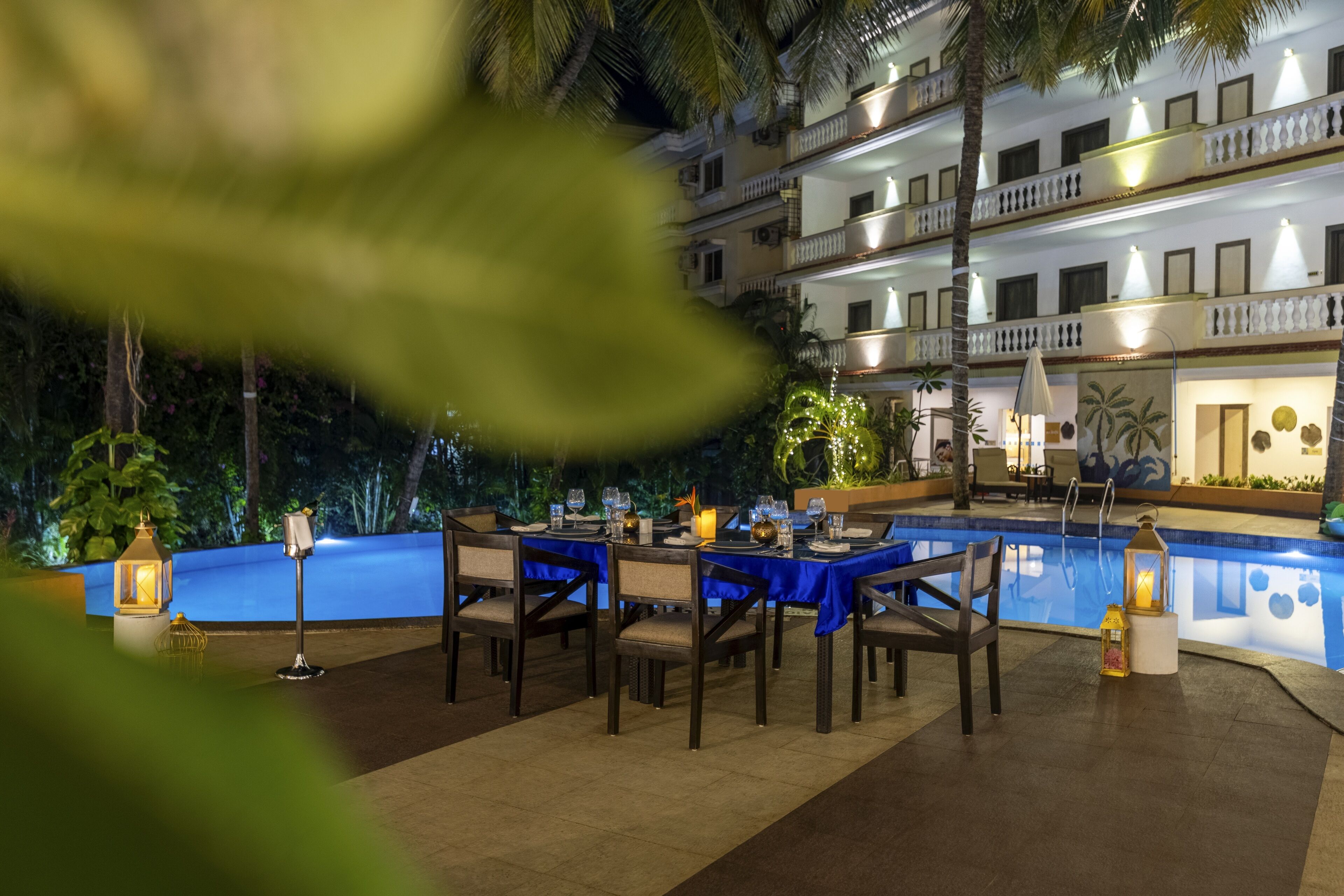 An outdoor dining area with tables and chairs, a pool, and a building with balconies in the background.
