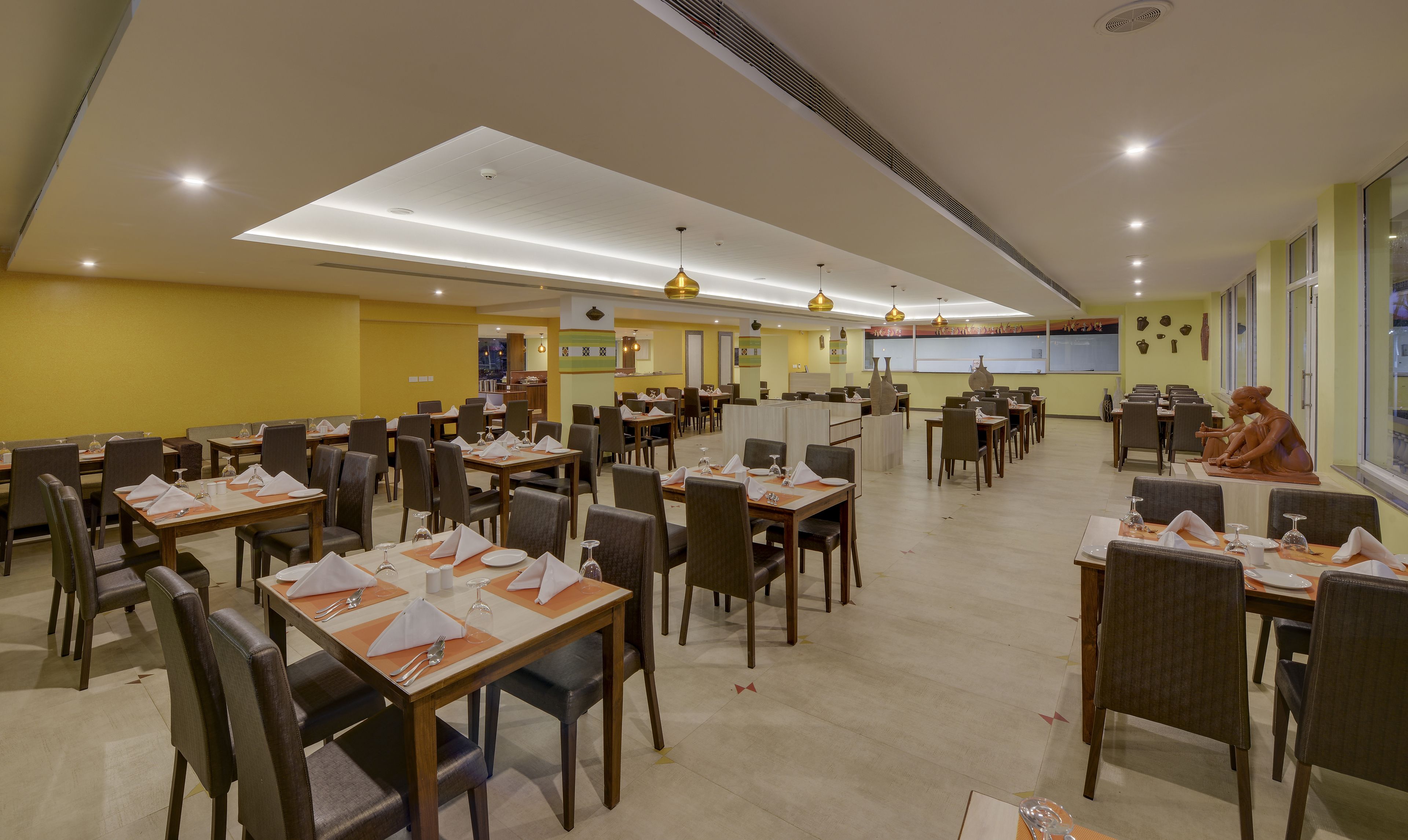 Um restaurante espaçoso com várias mesas e cadeiras, uma área de cozinha central e obras de arte decorativas nas paredes.
