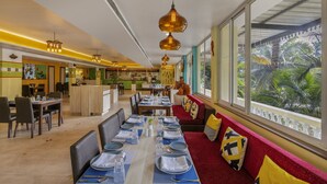A restaurant with a long dining table set for a meal, a bar area, and a seating area with a view of palm trees. - Sterling Goa Varca (Varca)