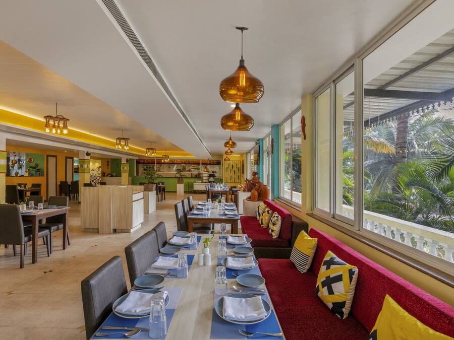 Un restaurante con una larga mesa de comedor lista para una comida, una zona de bar y un área de estar con vista a palmeras.