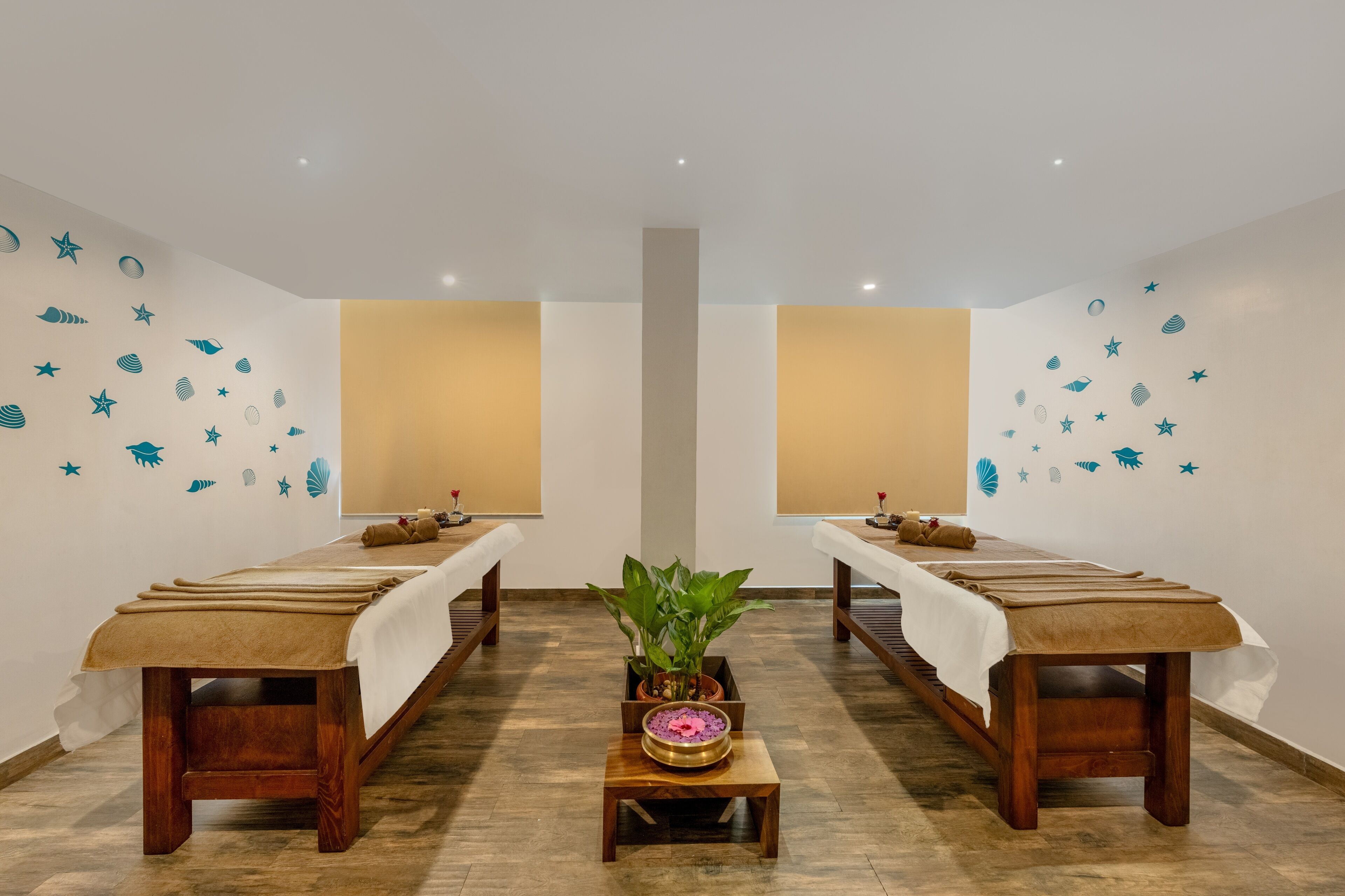 A spa room with two massage tables, a central plant, and decorative wall stickers.