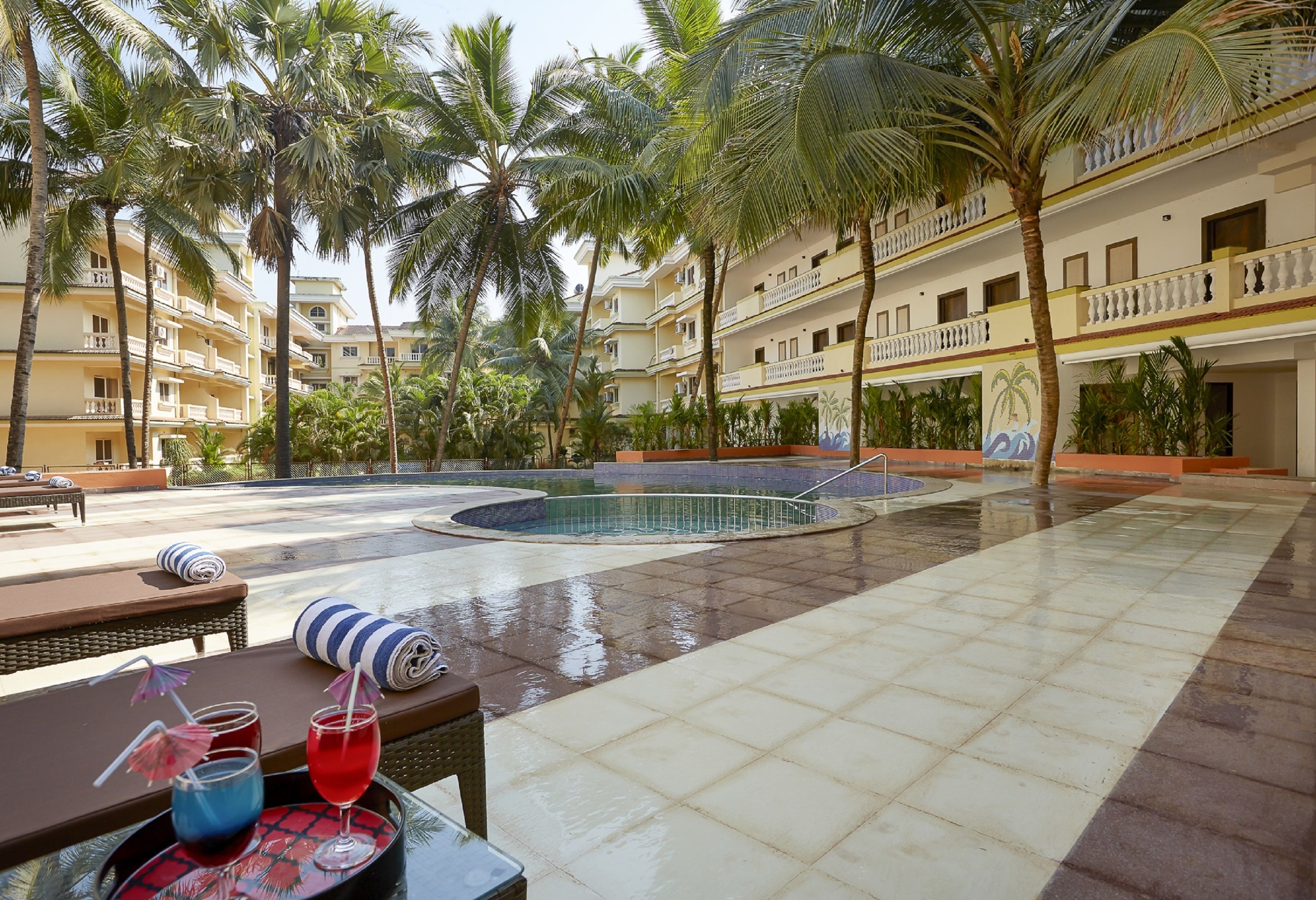 Un espace piscine d’hôtel agrémenté de palmiers, d’une piscine et de chaises longues.