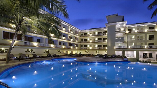 A hotel with a large pool, multiple balconies, and palm trees. - Sterling Goa Varca (Varca)