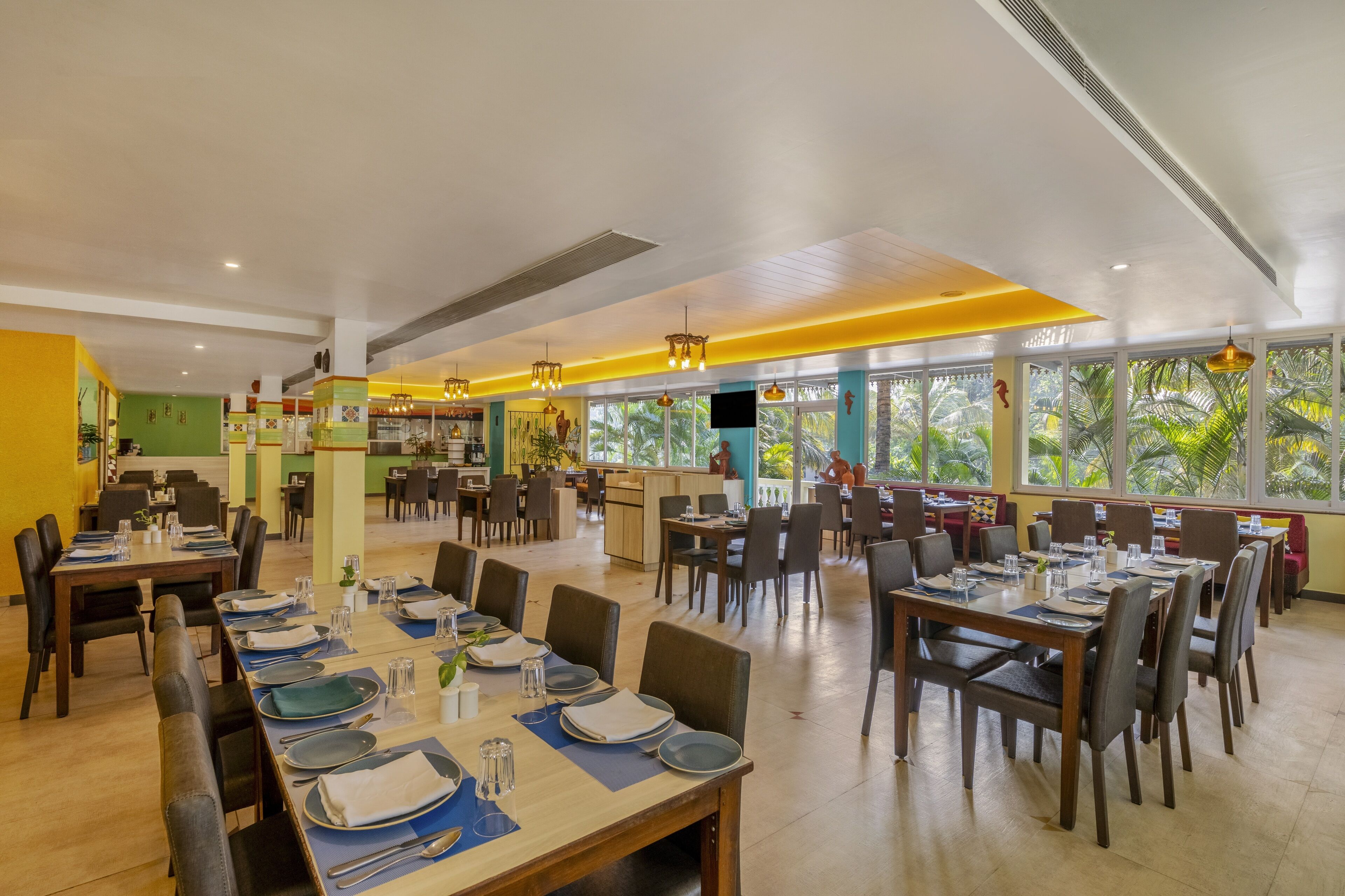 Um restaurante espaçoso com várias áreas de refeições, grandes janelas com vista para paisagens tropicais e um design de interiores moderno.