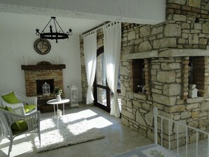 Um quarto aconchegante com lareira de pedra, um sofá de vime branco com almofadas verdes e um tapete branco.