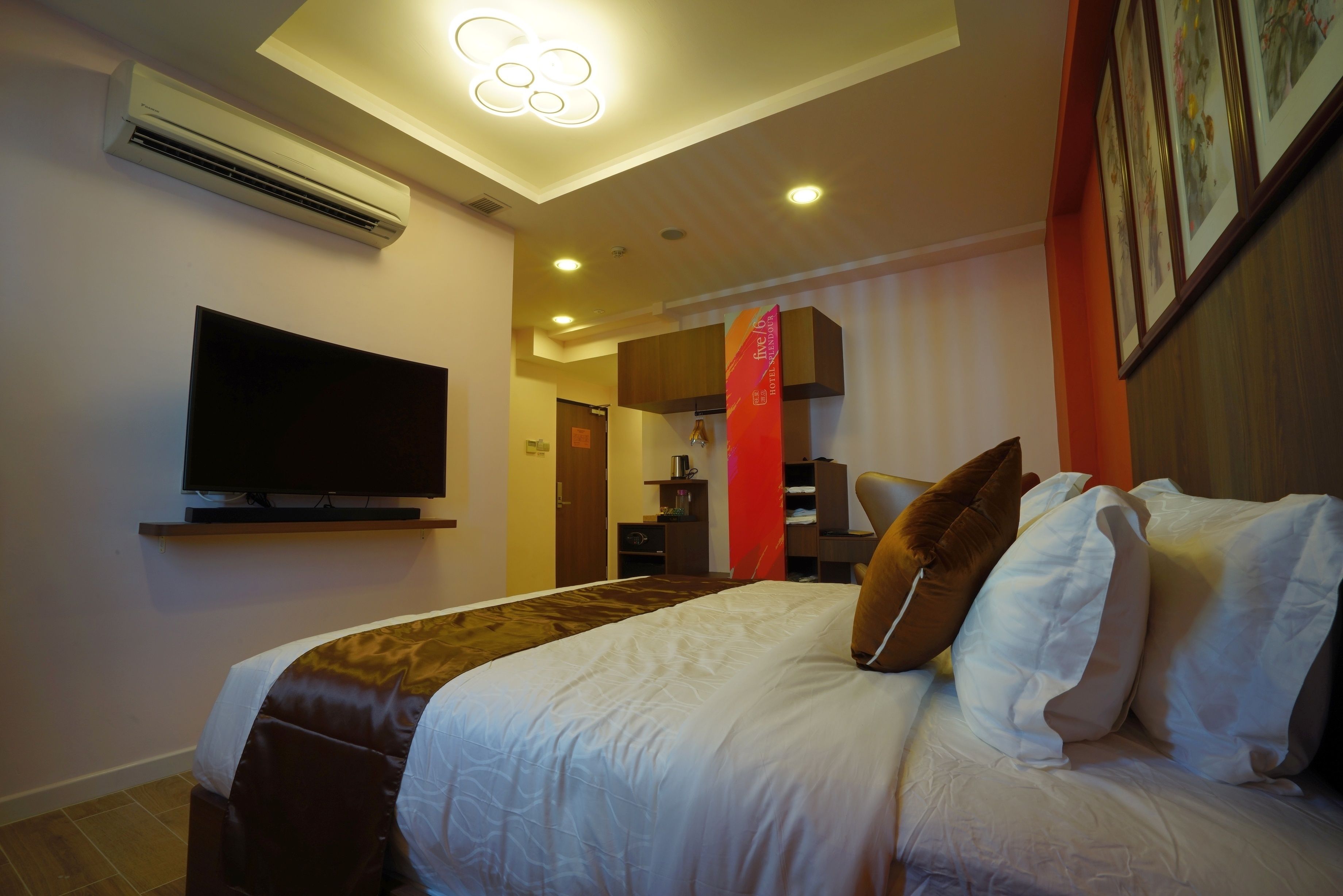 Ein Hotelzimmer mit Bett, einem an der Wand montierten Flachbildfernseher, einer roten Akzentwand und einer Deckenleuchte.