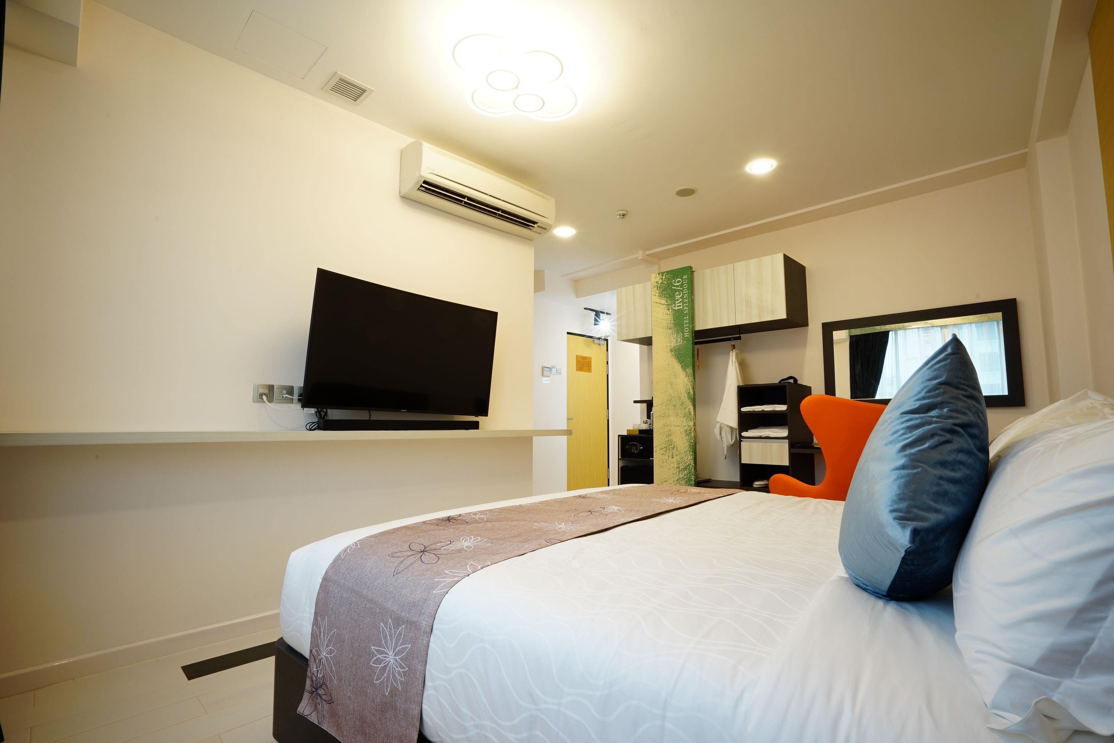 A hotel room with a bed, a flat-screen TV mounted on the wall, and a desk with a chair.
