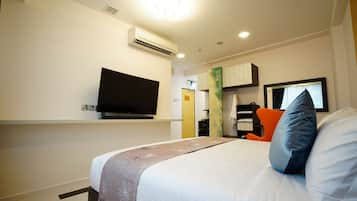 A hotel room with a bed, a flat-screen TV mounted on the wall, and a desk with a chair.