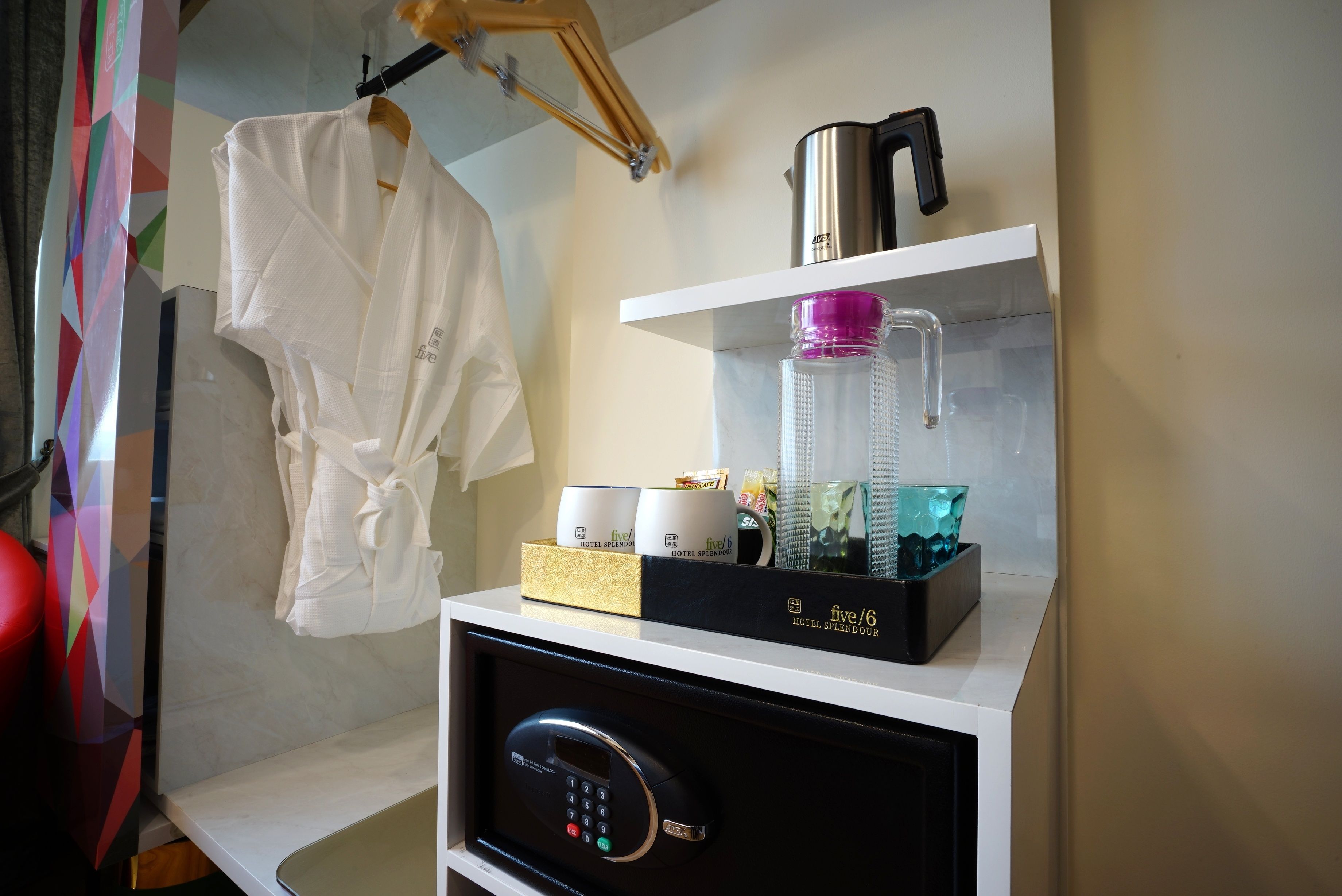 Mini-bar de hotel com painel de controle, uma garrafa de água e uma cafeteira.