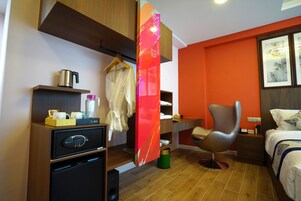 Una habitación de hotel moderna con un escritorio de madera, una silla, una cama y un minibar.