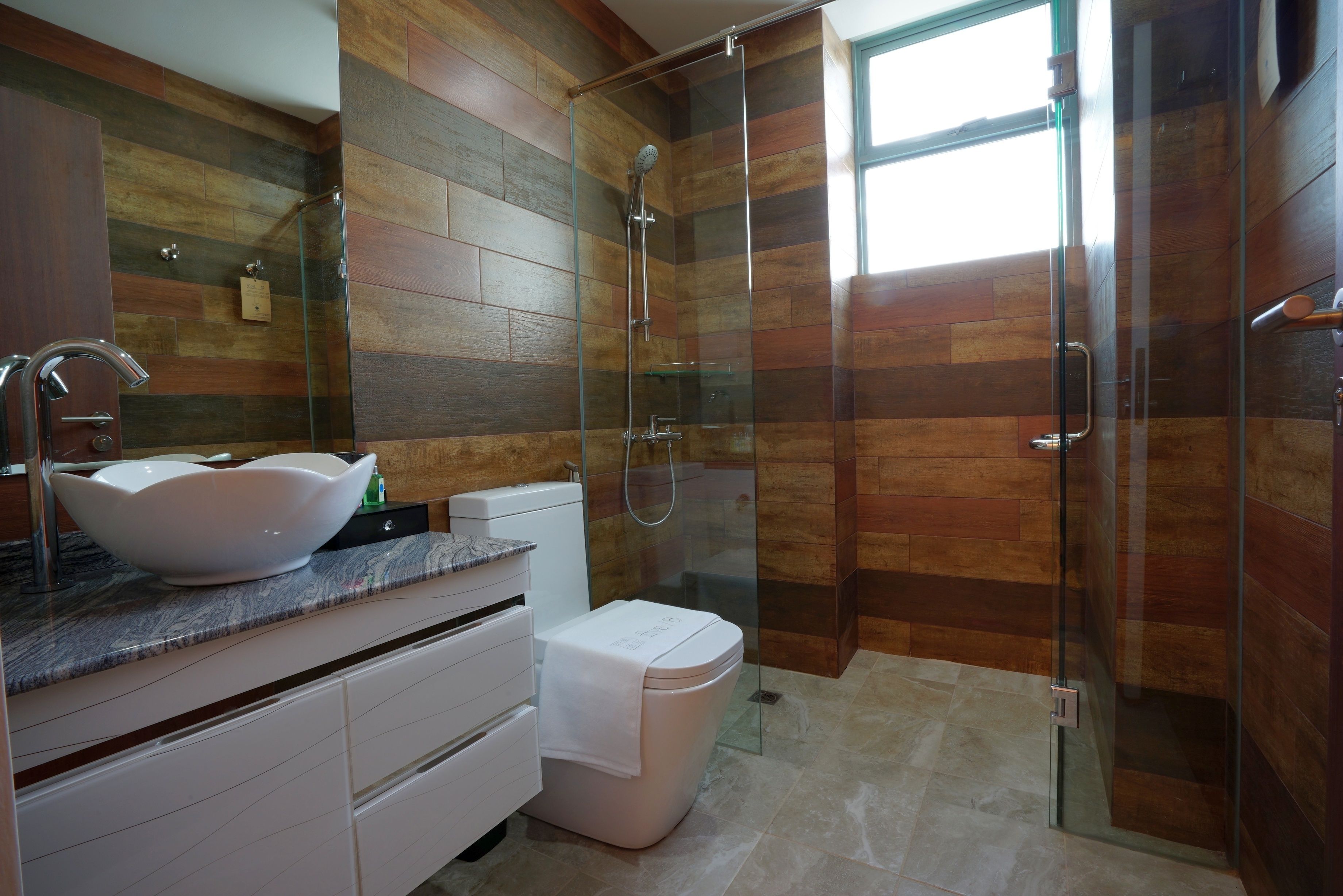 Un bagno moderno con doccia vetrata, lavandino bianco con bacinella ampia e mobile contenitore con cassetti.